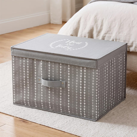 A gray fabric storage box with a heart pattern and "Neat and Tidy" on the lid, placed on a rug near a bed