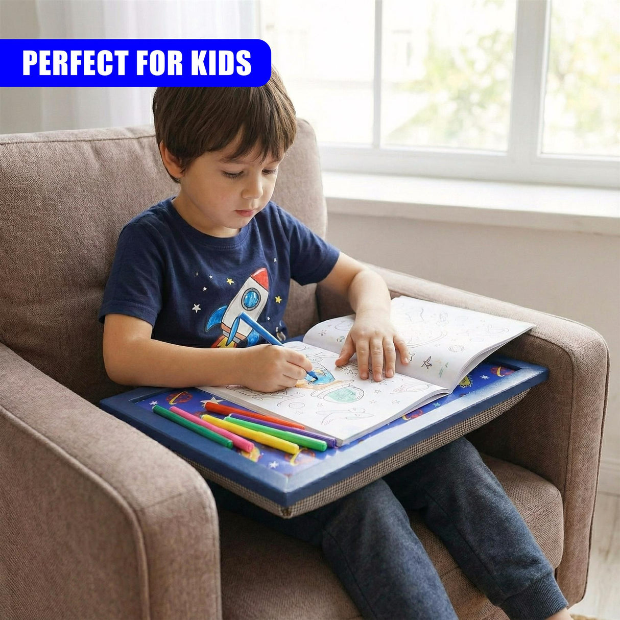 A boy writes on educational papers placed on a blue lap tray while seated on a couch.